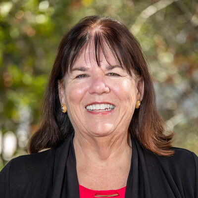 Dark-haired person with bangs wearing a red shirt and black blazer.