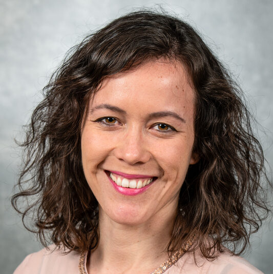Dark-haired person wearing a pink button-up top.