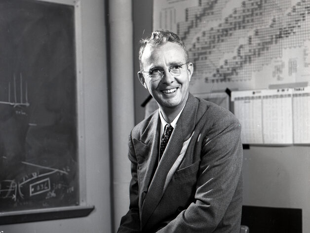 Short-haired person smiling in a suit and tie.