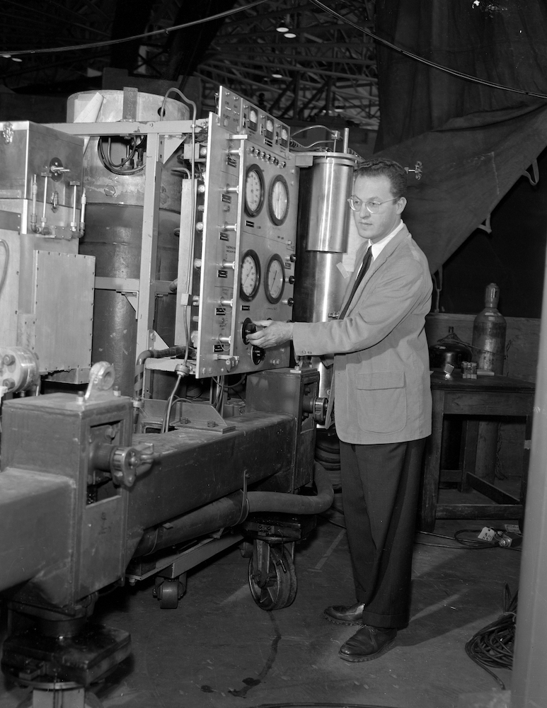 Person with short hair and glasses standing next to the xenon bubble chamber.