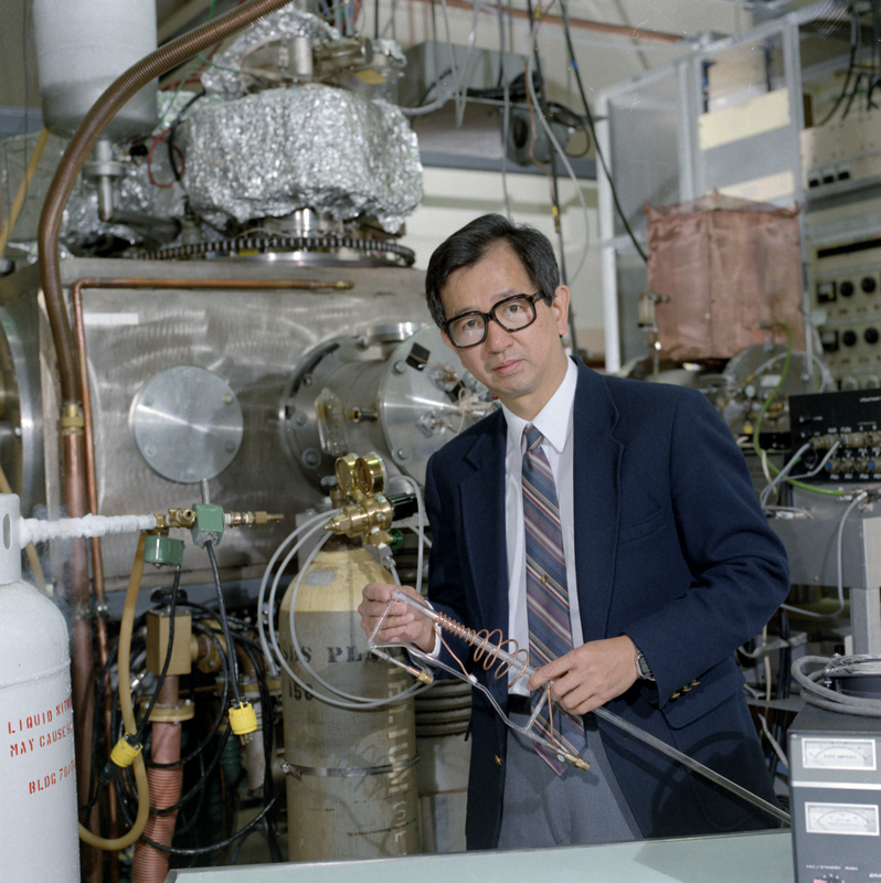 Dark-haired person in glasses standing in a room with machinery.
