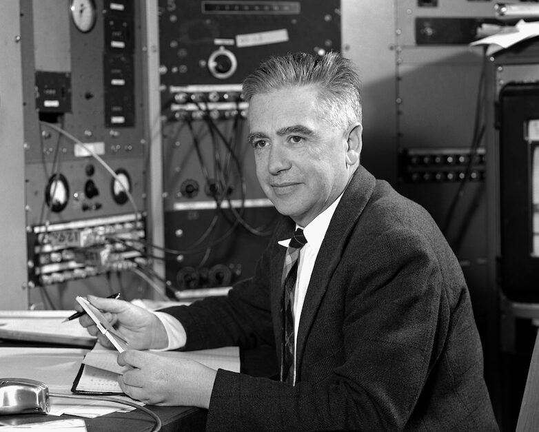 Dark-haired person wearing a black suit sitting in a lab space.