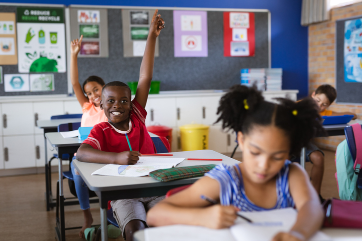 Boy and girl raising their hands while sitting in the class at elementary school.