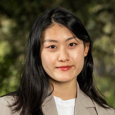 Dark-haired person wearing a white shirt and a beige blazer.