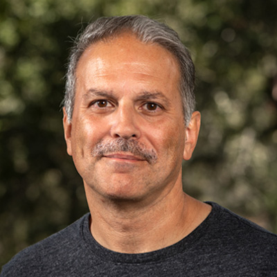 Dark-haired person with a mustache wearing a dark grey shirt.