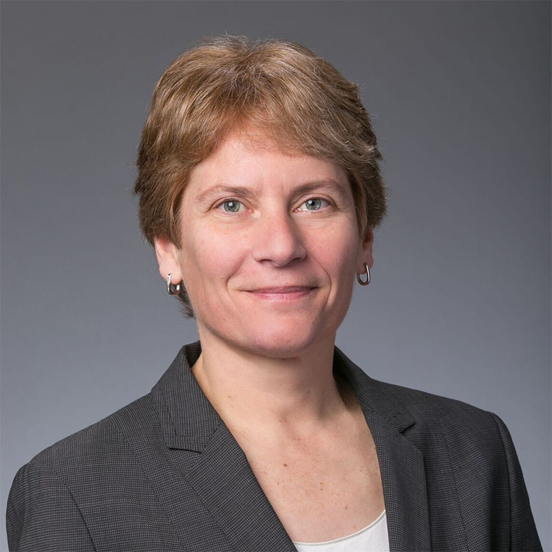 Light-haired person wearing a white shirt under a dark gray blazer.