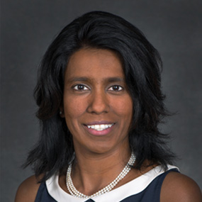 Dark-haired person wearing a pearl necklace and a collared shirt.