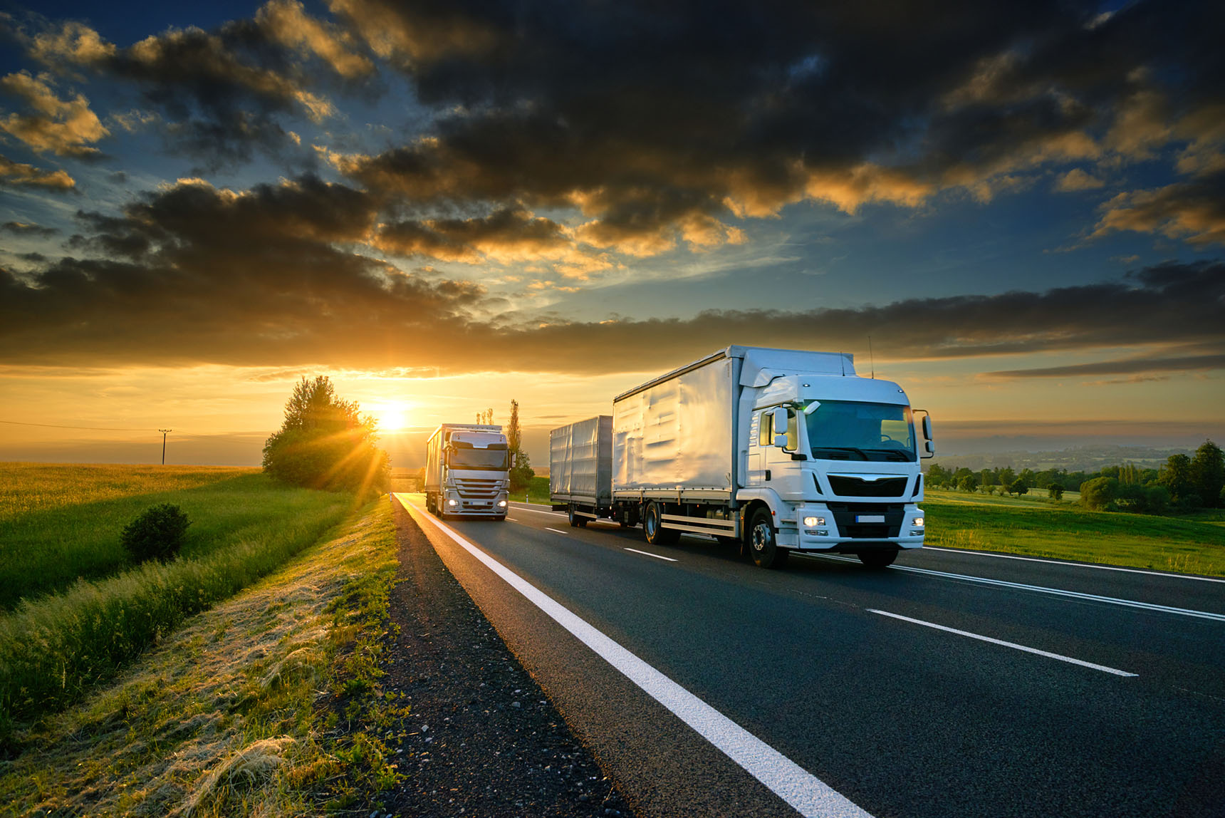 Trucks on an asphalt road in a rural landscape at sunset.