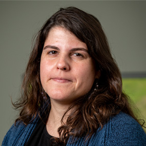 Person with mid-length dark hair wearing a black top and blue sweater.