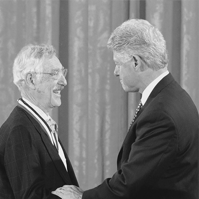 Two men in black suits standing toward each other.