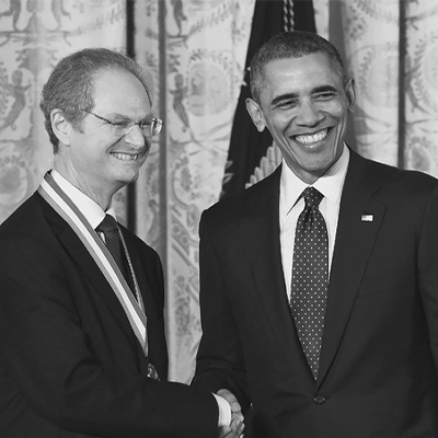 Two men in black suits shaking hands and looking toward the bottom right of the frame.