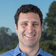 Person with short dark hair wearing a blue collared shirt outdoors.