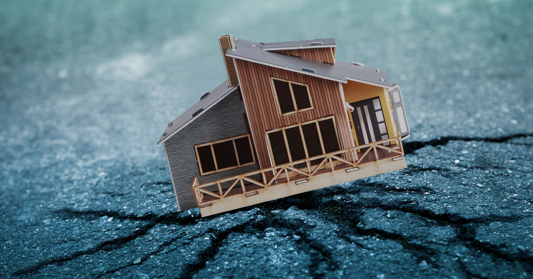 A small brown wooden model of a house sits on cracked concrete