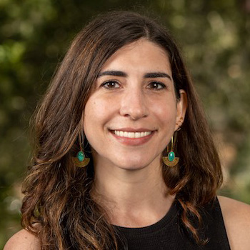 Person with long dark brown hair wearing a black top and colorful feathered earrings.