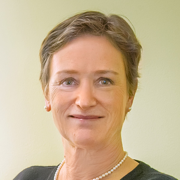 Person with short blonde hair wearing a dark top and a beaded necklace.