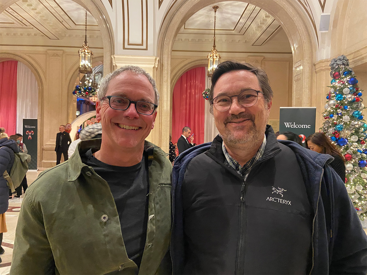 Two people with short hair and glasses standing next to each other for a photo in a foyer.