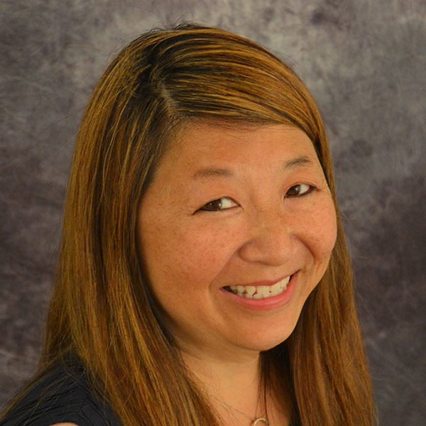 Smiling person with brown hair in front of a grey background.