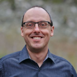 Person with short dark hair wearing glasses and a navy collared shirt.