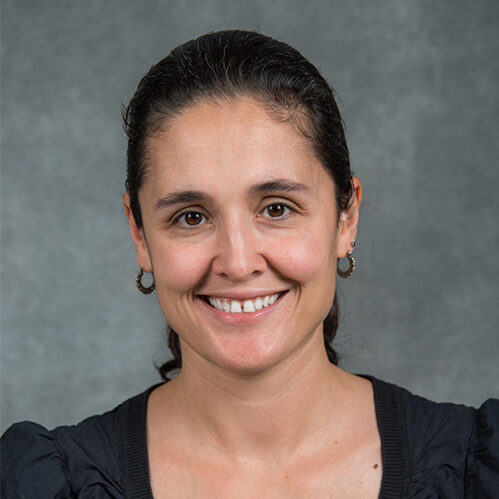 Person with dark hair pulled back wearing a black top, photographed against a gray backdrop.