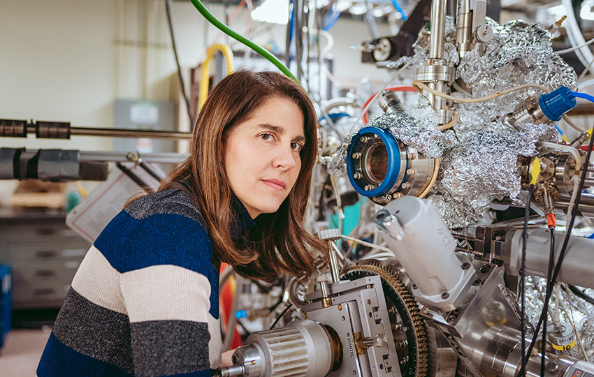 Person with long, brown hair standing in front of scientific instrumentation.