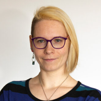 Cara Laasch, a person with short blonde hair, wearing glasses and a multicolored top.