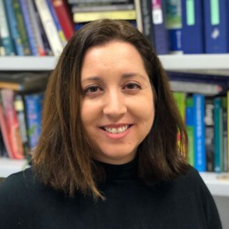 Michelle O'Malley, a person with medium-length brown hair wearing a black sweater, with rows of books in the background.