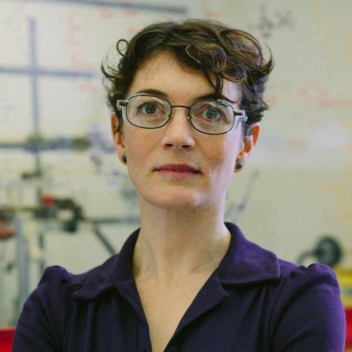 Polly Arnold, a person with short brown hair wearing glasses and a purple collared top, photographed in a lab.