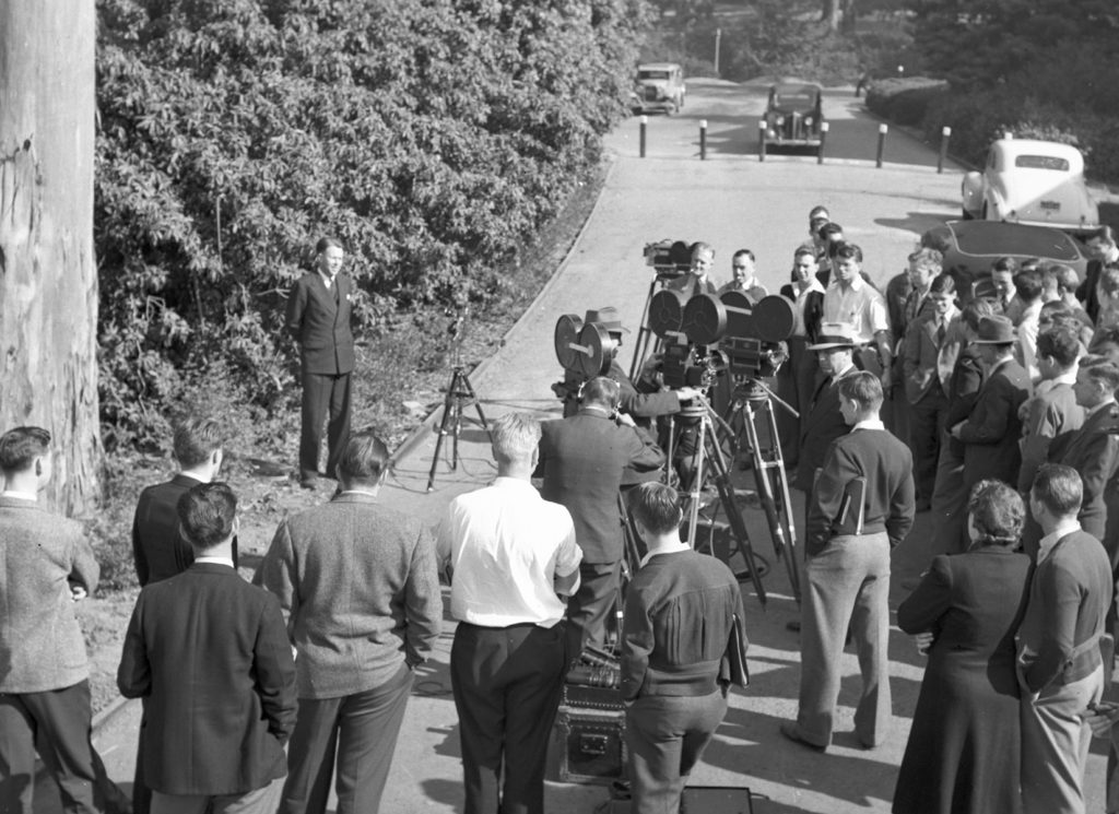 Large group of individuals and media equipment surrounding Ernest Lawrence for a press interview.
