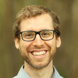 Benjamin Nachman, a person with short blonde hair wearing glasses and a gray collared shirt.