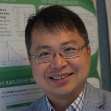 Alan Poon, a person with short black hair wearing glasses and a gray collared jacket over a checkered collared shirt. Posing in front of a poster board.
