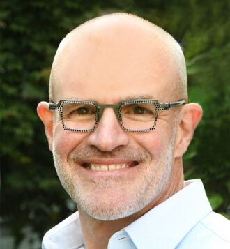 Jay Keasling, a short-haired person wearing glasses, smiles for a headshot outdoors.