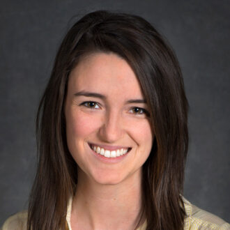 Sarah Smith, a person with medium-length brown hair wearing a light collared top, photographed against a gray backdrop.