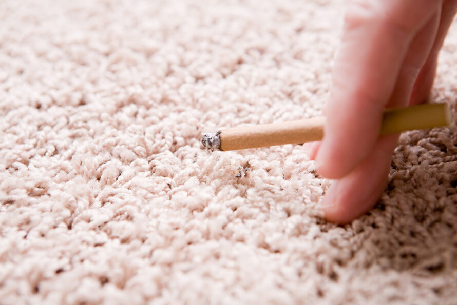 Fingers holding a cigarette near a beige carpet.