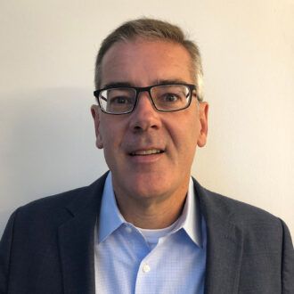 Jeffrey Long, a person with short gray hair wearing glasses and a gray blazer over a blue and white checkered collared shirt. Photographed against a beige wall.