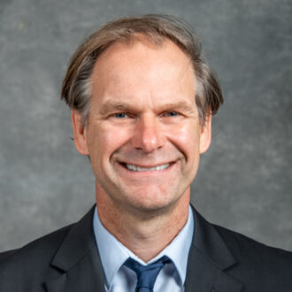 Thomas Schenkel, a senior scientist in Berkeley Lab’s Accelerator Technology & Applied Physics (ATAP) Division. Schenkel has short gray hair and is wearing a suit and tie, photographed in front of a gray backdrop.