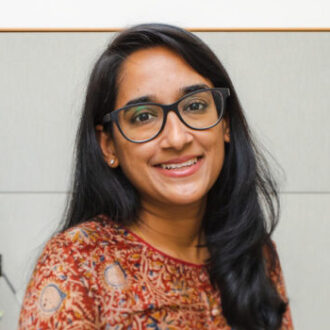 Archana Raja, a person with long dark hair wearing a red patterned shirt.