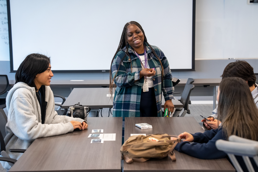 Three students sitting at a desk in conversation with Faith Dukes, a person standing. High School students participate in Science en Acción (SeA), a free STEM camp at Lawrence Berkeley National Laboratory for English learning and Spanish-English bilingual students who are interested in science, technology, engineering and mathematics (STEM).