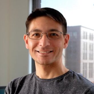 Michael Smitasin, a person with short dark hair wearing glasses and a gray shirt, photographed indoors.