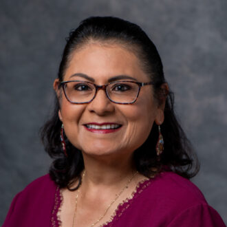 Portrait of Rosa Rodriguez Flores, a person with short dark hair wearing glasses and a dark red blouse.