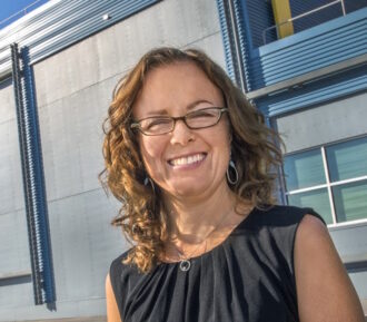 Cindy Regnier, a person with medium-length brown hair wearing glasses and a black top, in front of FLEXLAB.