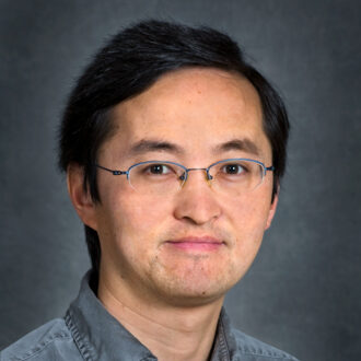 Yuxin Wu, a person with short dark hair, wearing glasses and a dark blue gray collared shirt. Photographed in a studio.