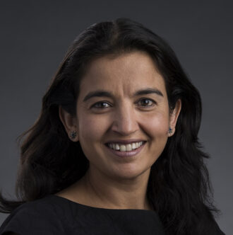 A portrait of Harshini Mukundan, a person with medium-length dark hair wearing a black top.