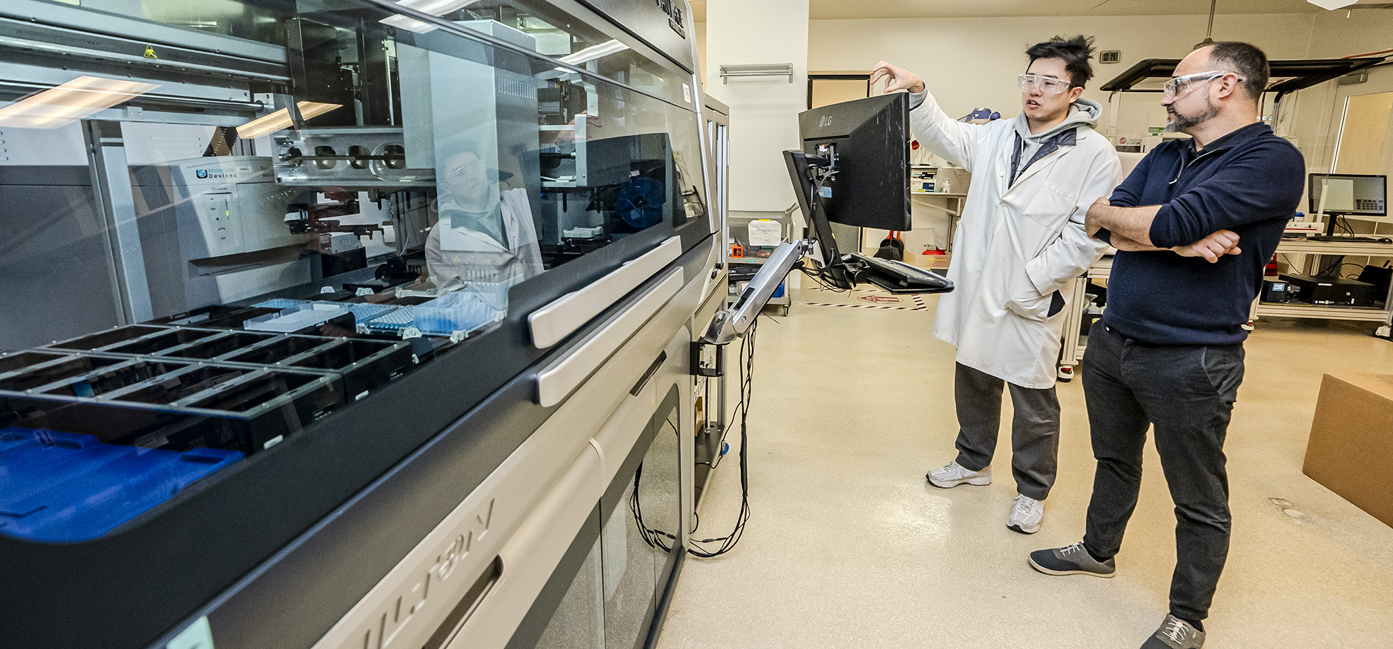 Two people standing on the right side of an automated lab.