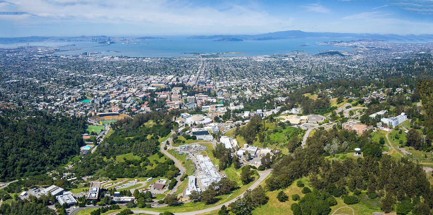 Birdseye view of green hills and Berkeley Lab in front of the Bay waters and blue skies.