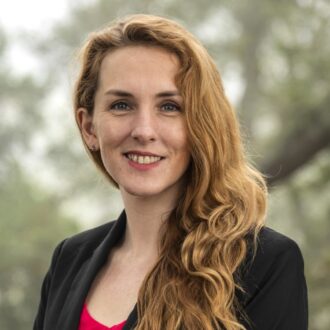 Jennifer Pore, a person with long blonde hair wearing a black blazer over a red top, photographed outdoors.
