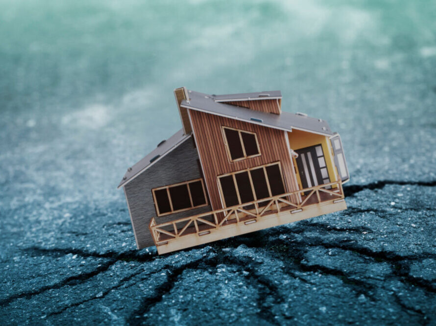 A small brown wooden model of a house sits on cracked concrete.