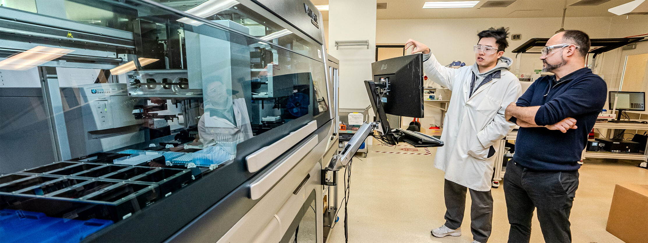 Two scientists standing to the right of an automated lab.