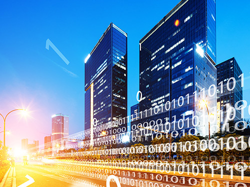 Modern cityscape at dusk with tall commercial buildings and traffic below. Digital overlay of white binary code stream towards the city.