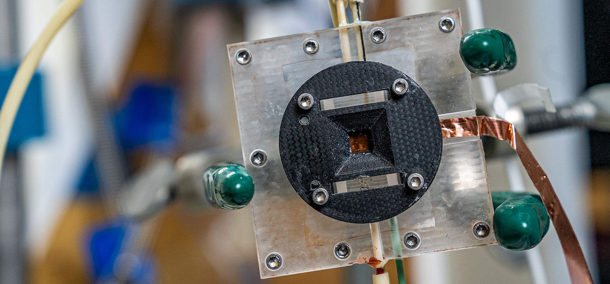 Close-up of a square metal and plastic lab component with tubes and copper wiring connected.