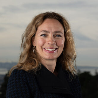 Kristin Persson, a person with medium-length dark blonde hair wearing a black top with silver earrings, smiling.